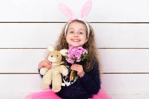 happy girl in bunny ears with easter rabbit toy, flowers