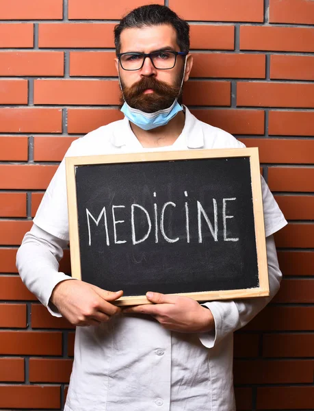 Barbudo brutal caucasiano médico segurando bordo com "Medicina" inscrição — Fotografia de Stock