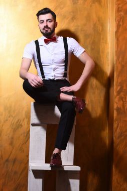 Sakallı adam ciddi yüzüyle sandalyede oturuyor.