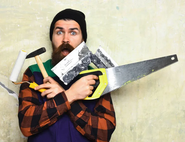 Bärtiger Arbeiter mit verschiedenen Bauwerkzeugen und überraschtem Gesicht — Stockfoto