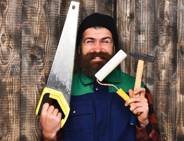 Bebaarde bouwer houden verschillende gebouw tools met blij gezicht — Stockfoto