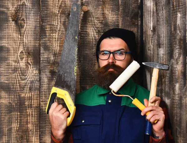 Brodaty malarz trzymający różne narzędzia budowlane o poważnej twarzy — Zdjęcie stockowe