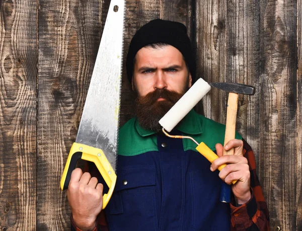 Бородатый человек держит различные строительные инструменты с серьезным лицом — стоковое фото