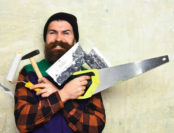 Brodaty mężczyzna trzyma różne narzędzia budowlane ze szczęśliwą twarzą — Zdjęcie stockowe