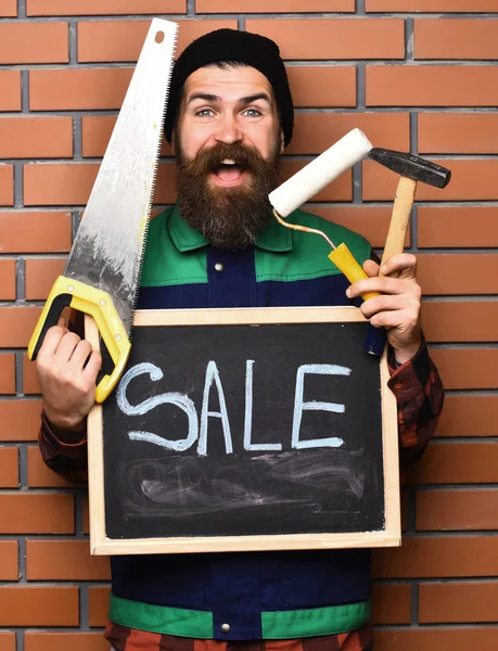 Barbudo hombre sosteniendo varias herramientas de construcción y tablero, cara feliz —  Fotos de Stock