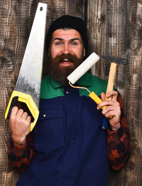 Construtor barbudo segurando várias ferramentas de construção com rosto feliz — Fotografia de Stock