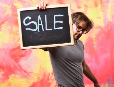 Beyaz sakallı seksi maço adam elinde satılık bir yazı tutuyor.