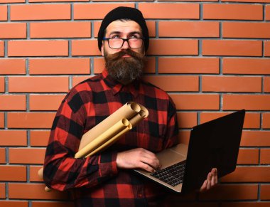 Kaba sakallı, beyaz tenli hippi elinde dizüstü bilgisayar ve el işi kâğıdı tutuyor.