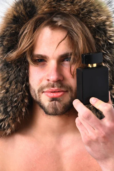 Bearded macho man in fur coat holding perfume bottle — Stock Photo, Image