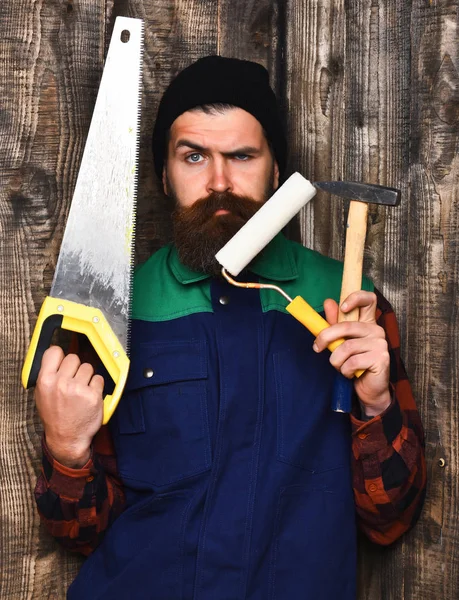 Homem barbudo segurando várias ferramentas de construção com rosto sério — Fotografia de Stock