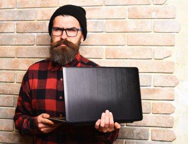 Kaba sakallı, beyaz tenli hippi dizüstü bilgisayar tutuyor.