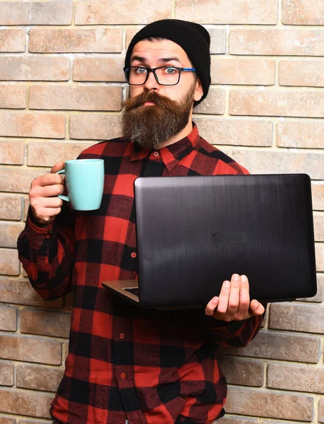 Brutalny, biały hipster trzymający laptopa z kubkiem — Zdjęcie stockowe