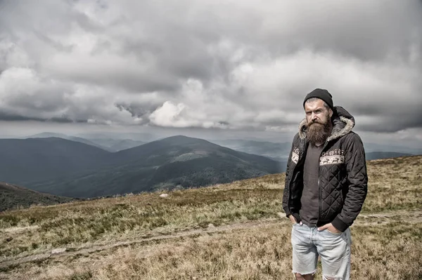 Hipster, bärtiger Mann auf einem Berggipfel am wolkenverhangenen Himmel — Stockfoto