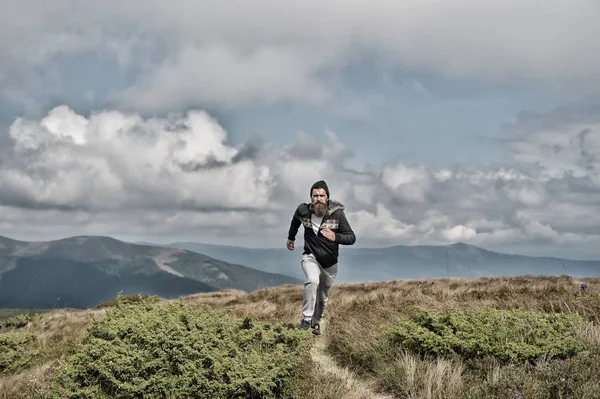Человек бежит по зеленому лугу в горах на облачном небе — стоковое фото