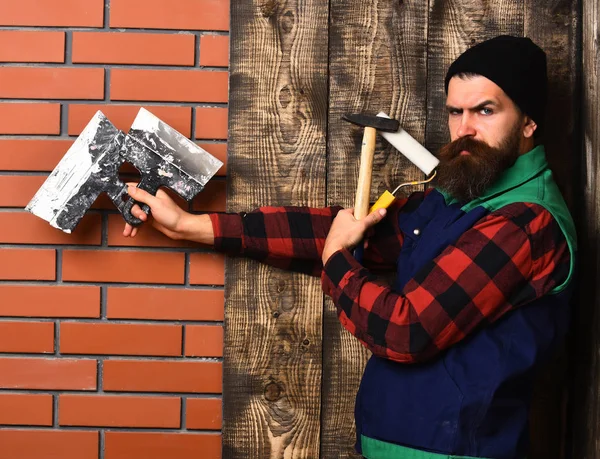 Бородатый мастер держит различные строительные инструменты с серьезным лицом — стоковое фото