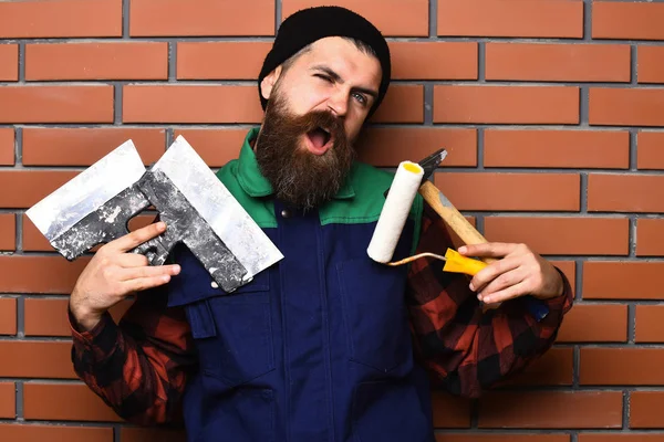 Бородатий будівельник тримає різні будівельні інструменти з задоволеним обличчям — стокове фото