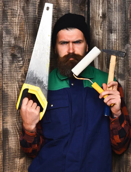 Бородатый человек держит различные строительные инструменты с серьезным лицом — стоковое фото