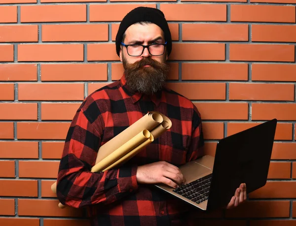 Бородатий жорстокий білий хіпстер тримає ноутбук і ремісничий папір — стокове фото