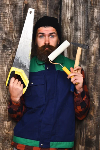 Бородатый строитель держит различные строительные инструменты с удивленным лицом — стоковое фото