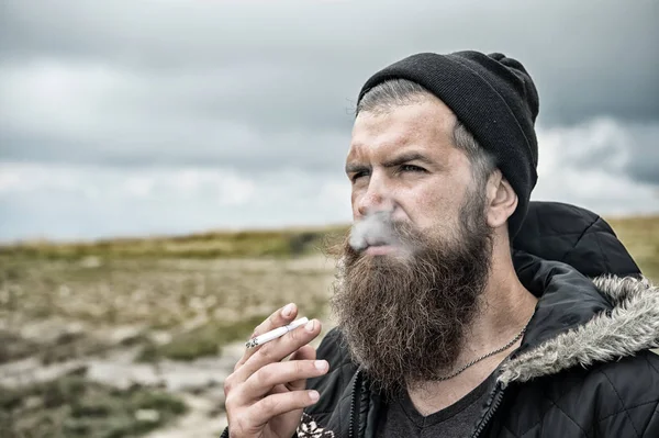 Homem com barba fumando cigarro na montanha, céu nublado — Fotografia de Stock