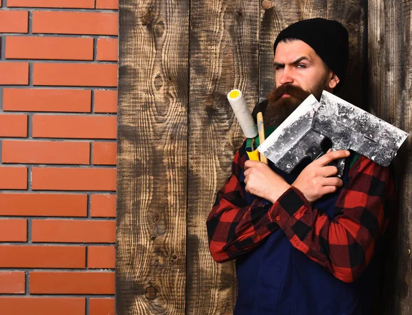 Бородатый мастер держит различные строительные инструменты с серьезным лицом — стоковое фото
