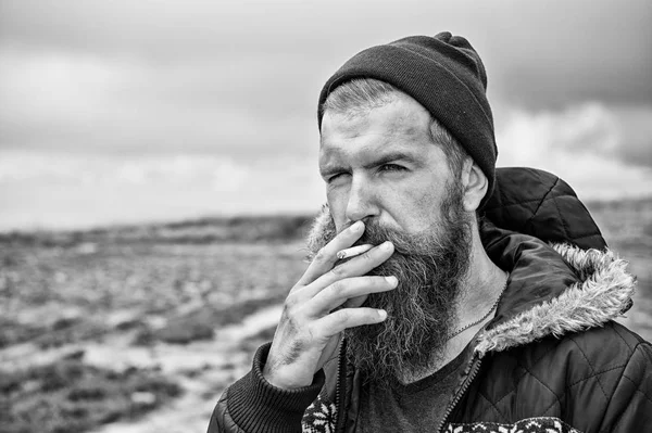 Mannen med skägg rökning cigarett på berg, molnig himmel — Stockfoto