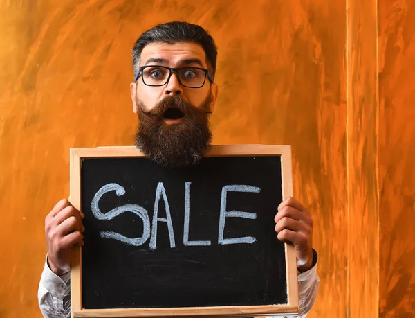 留着胡子的男人，残忍的高加索嬉皮士，在黑板上拿着销售题词 — 图库照片