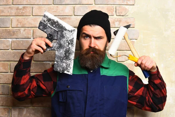 Vousatý stavitel muž drží různé stavební nástroje s vážnou tváří — Stock fotografie