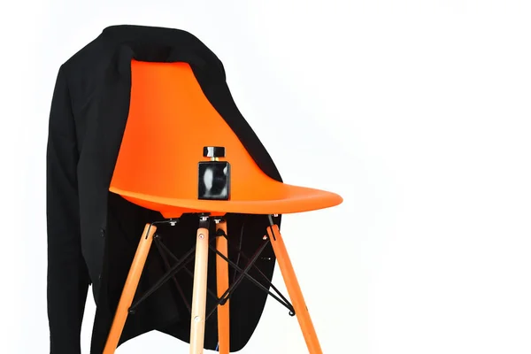 Оранжевый пластиковый офисный стул с черной курткой и флаконом духов — стоковое фото