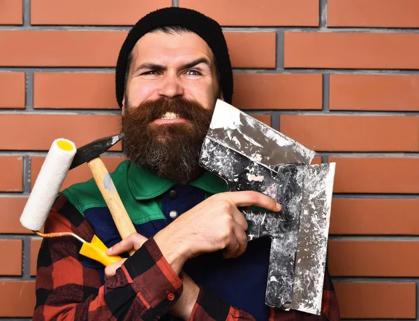Бородатий будівельник тримає різні будівельні інструменти з щасливим обличчям — стокове фото