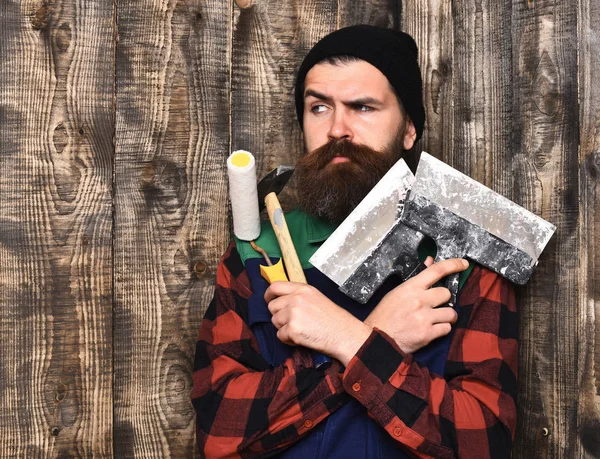 Homem pintor barbudo segurando várias ferramentas de construção com rosto sério — Fotografia de Stock