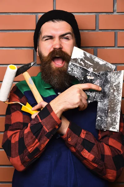 Γενειοφόρος οικοδόμος άνθρωπος κρατώντας διάφορα εργαλεία κτίριο με χαρούμενο πρόσωπο — Φωτογραφία Αρχείου