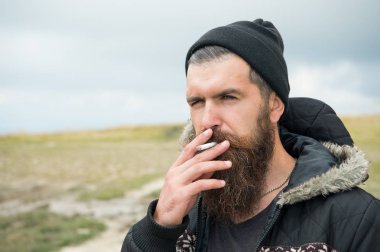 Genç sakallı hippi adam duman sigara Mountain, bulutlu gökyüzü