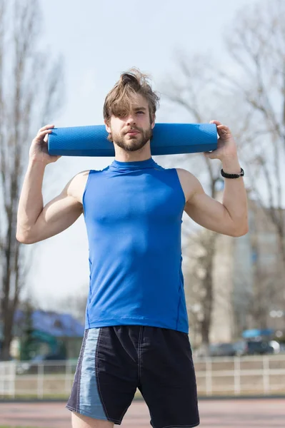 Йога, фітнес килимок синього кольору в руках м'язистого чоловіка — стокове фото