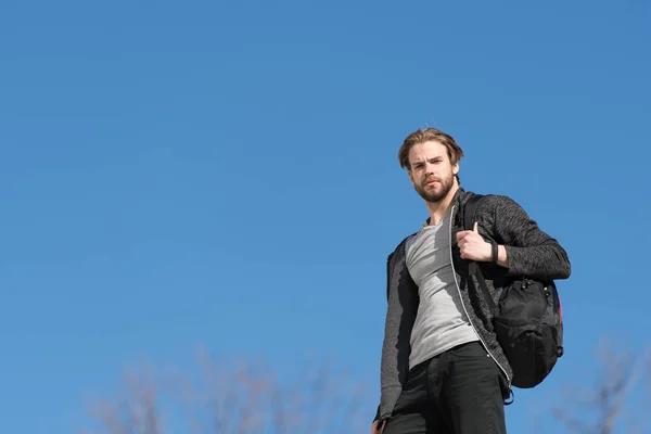 Вдумчивый молодой человек на фоне голубого неба со спортивной сумкой — стоковое фото
