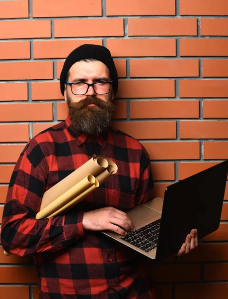 Bearded brutal caucasian hipster holding laptop and craft paper — Stock Photo, Image