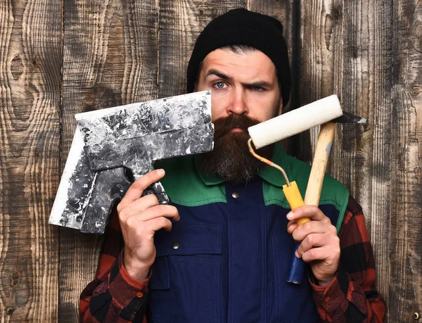 Homem construtor barbudo segurando várias ferramentas de construção com rosto sério — Fotografia de Stock