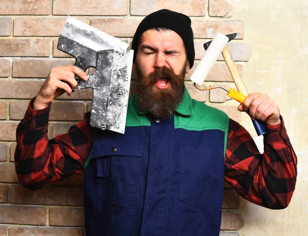 Homem pintor barbudo segurando várias ferramentas de construção com rosto satisfeito — Fotografia de Stock