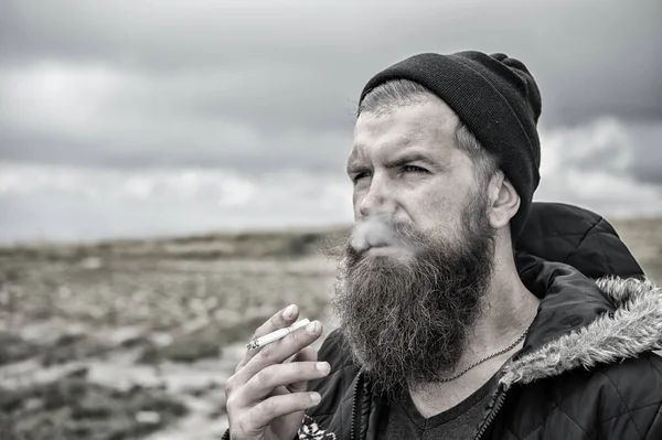 Barbudo hipster con barba larga fumar cigarrillo en sombrero al aire libre — Foto de Stock