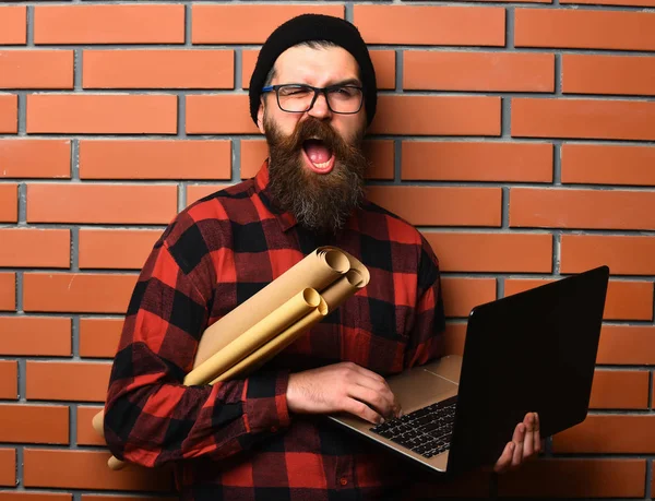 Bearded brutal caucasian hipster holding laptop and craft paper — Stock Photo, Image