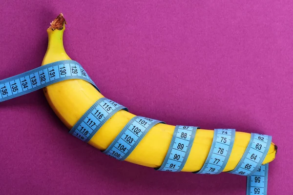 Banana with measuring tape on purple background — Stock Photo, Image