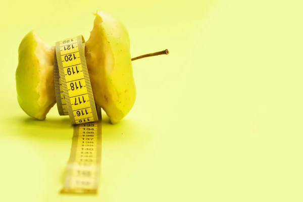 Tejp för att mäta band runt bitten äpple på gul bakgrund — Stockfoto