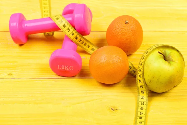 Fruit and health concept, dumbbells weight with measuring tape — Stock Photo, Image