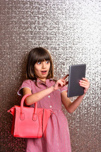 Pequeña linda chica sorprendida con bolsa de cuero rojo y tableta — Foto de Stock