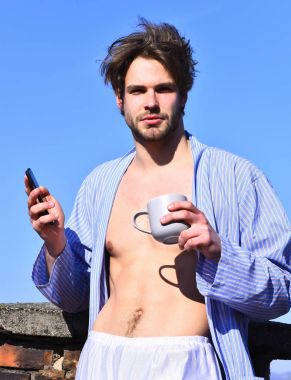 Mavi çizgili pijamalı, elinde fincanla beyaz maço.