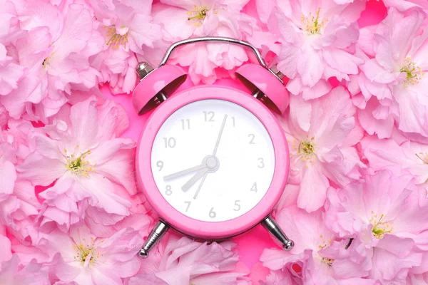Alarm clock in bright pink colour and blooming sakura flowers — Stock Photo, Image