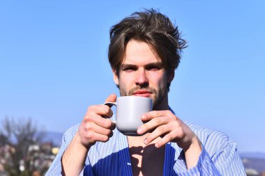 Mavi çizgili pijamalı, elinde fincanla beyaz maço.