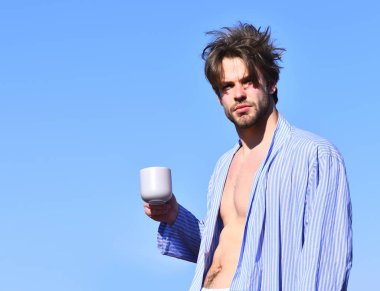 Mavi çizgili pijamalı, elinde fincanla beyaz maço.