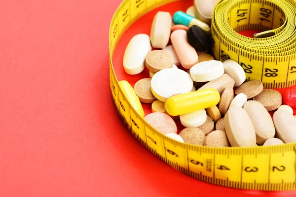 Рулон измерительной ленты обертывания вокруг лекарств на красном фоне — стоковое фото