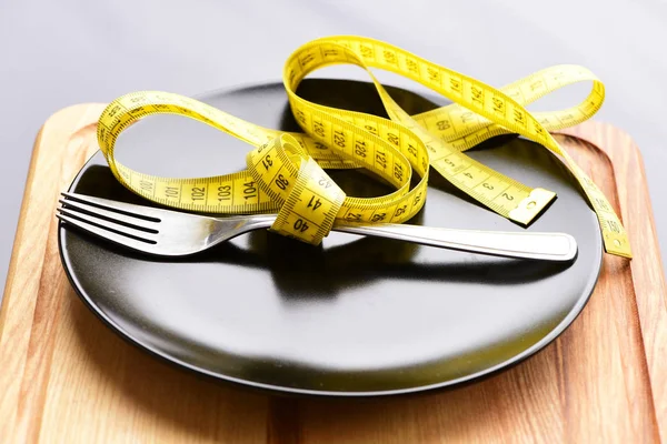 Yellow measure tape belted around metal fork on black plate — Stock Photo, Image